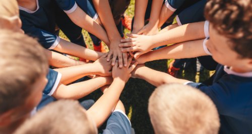 Squadra di giovani atleti con le mani unite al centro del campo